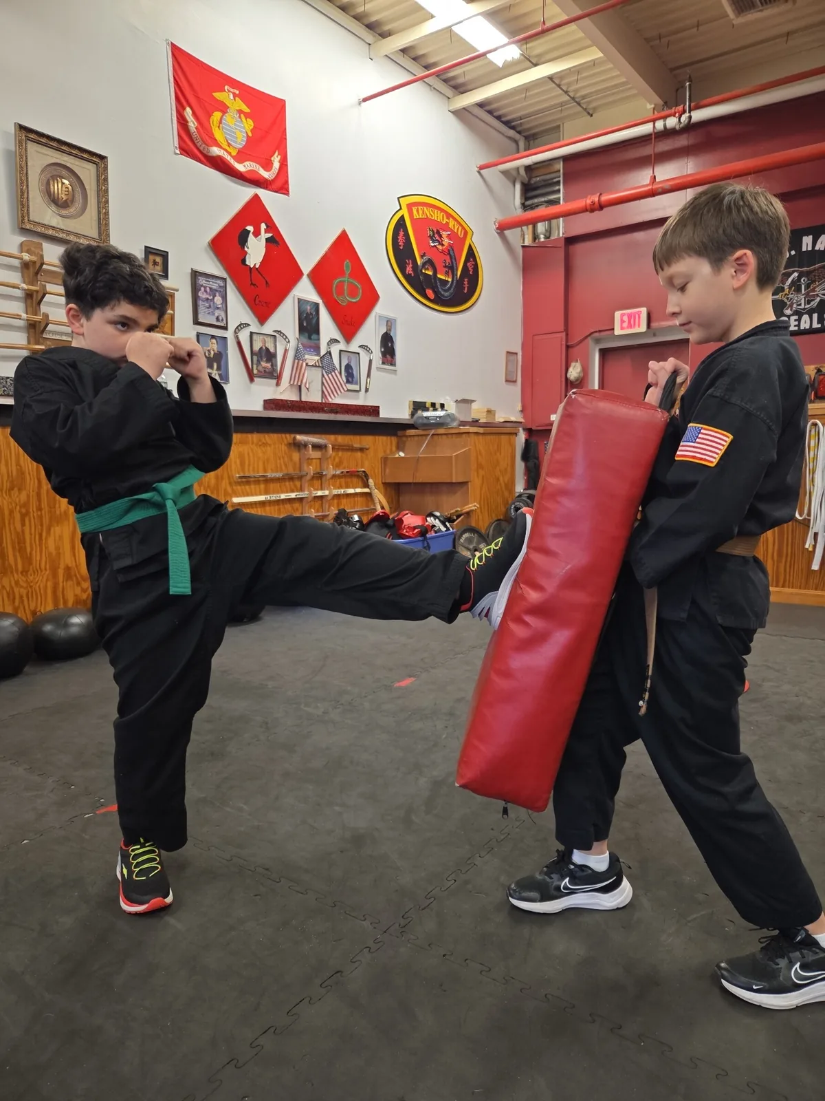 Two Zanshin youth students practicing a kick with a training shield in the dojo